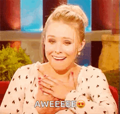 A Woman Is Smiling And Holding Her Hand To Her Chest While Wearing A Polka Dot Shirt . GIF