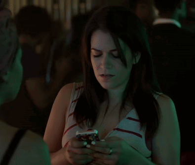 A Woman Is Smiling And Looking At Her Phone In A Dark Room GIF