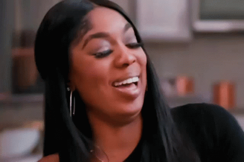 A Woman Is Smiling And Making A Funny Face While Wearing A Black Shirt And Earrings . GIF