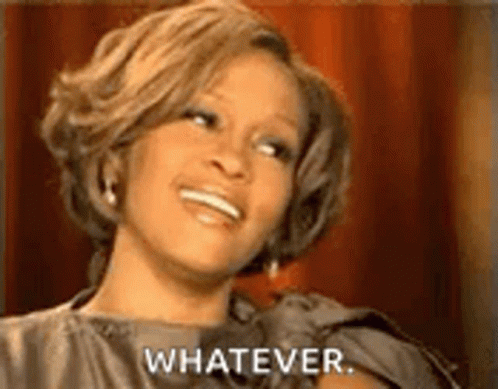 A Woman Is Smiling And Saying `` Whatever '' While Sitting In Front Of A Red Curtain . GIF