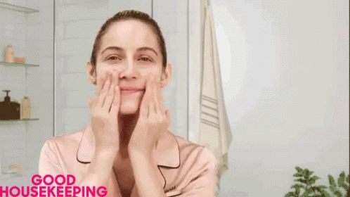 A Woman Is Smiling And Touching Her Face In Front Of A Clock That Says Anti-Aging Niacinamide Hyaluronic Acid GIF