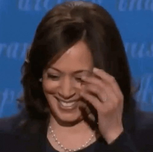 A Woman Is Smiling And Touching Her Face With Her Hand While Wearing A Pearl Necklace . GIF