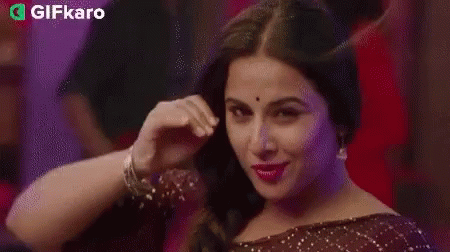 A Woman Is Smiling And Touching Her Hair In A Braid . GIF