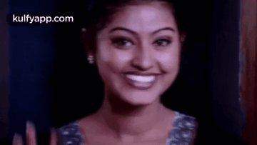 A Woman Is Smiling And Waving Her Hand In Front Of A Dark Background . GIF