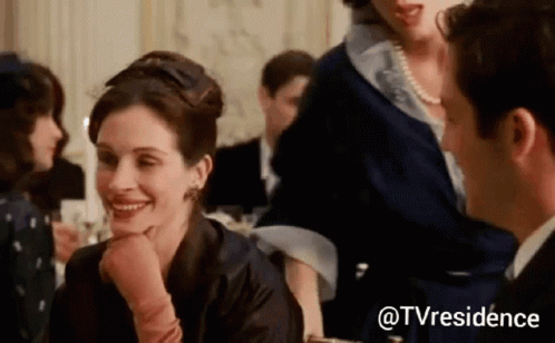 A Woman Is Smiling At A Man While Sitting At A Table In A Crowded Room . GIF