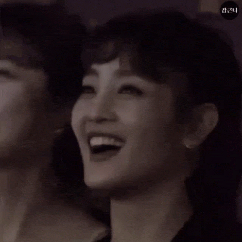 A Woman Is Smiling In A Black And White Photo . GIF