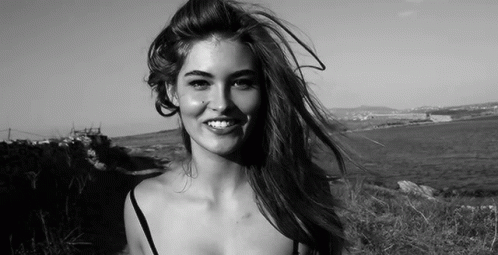 A Woman Is Smiling In A Black And White Photo While Her Hair Is Blowing In The Wind . GIF