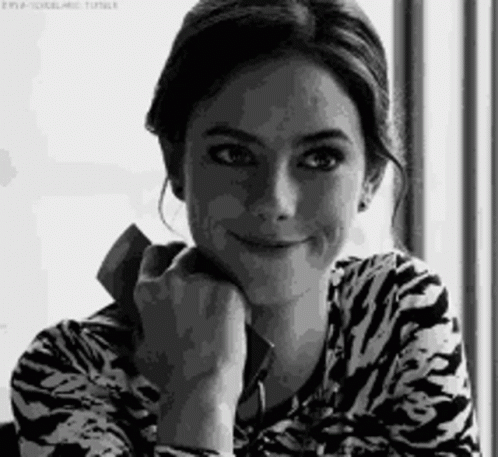 A Woman Is Smiling In A Black And White Photo While Holding A Cell Phone . GIF