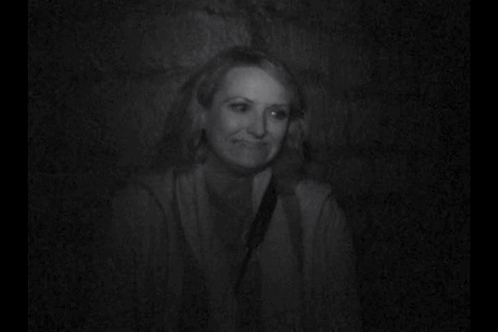 A Woman Is Smiling In A Black And White Photo While Sitting In A Dark Room . GIF