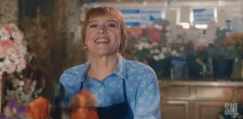 A Woman Is Smiling In A Flower Shop While Holding Flowers . GIF