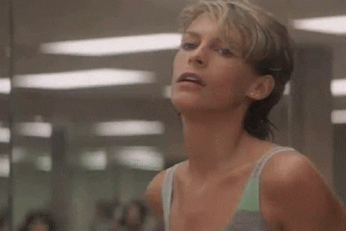 A Woman Is Smiling In A Gym While Wearing A Tank Top . GIF
