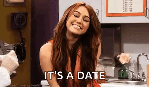 A Woman Is Smiling In A Kitchen With The Words `` It 'S A Date '' Written On Her Face . GIF