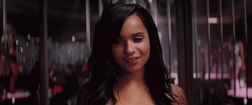A Woman Is Smiling In Front Of A Crowd Of People In A Dark Room . GIF