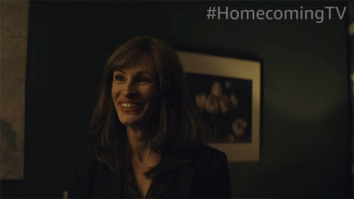 A Woman Is Smiling In Front Of A Framed Picture With #Homecomingtv Written On The Bottom GIF