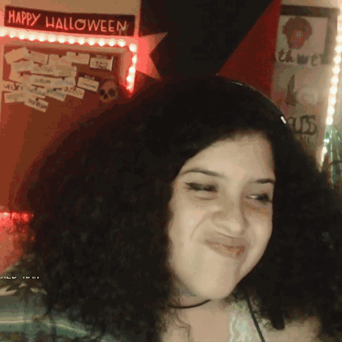 A Woman Is Smiling In Front Of A Happy Halloween Sign GIF