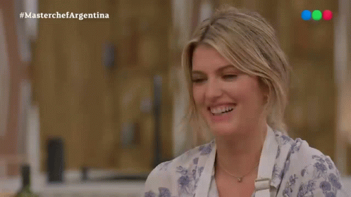A Woman Is Smiling In Front Of A Masterchef Argentina Sign GIF