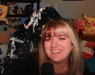 A Woman Is Smiling In Front Of A Microphone In A Room Filled With Toys . GIF