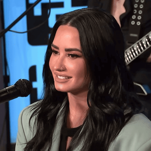A Woman Is Smiling In Front Of A Microphone With A Guitar In The Background GIF