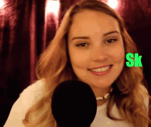 A Woman Is Smiling In Front Of A Microphone With The Letters Sk On Her Face GIF