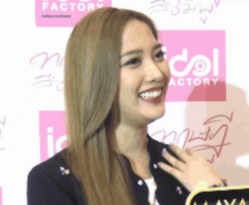 A Woman Is Smiling In Front Of A Pink Sign That Says Idol Actory GIF