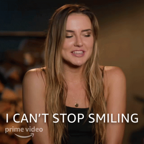 A Woman Is Smiling In Front Of A Sign That Says I Can 'T Stop Smiling Prime Video GIF