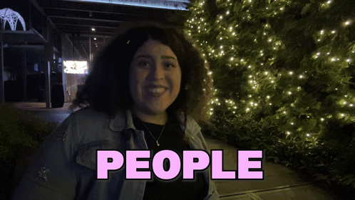 A Woman Is Smiling In Front Of A Sign That Says " People " GIF