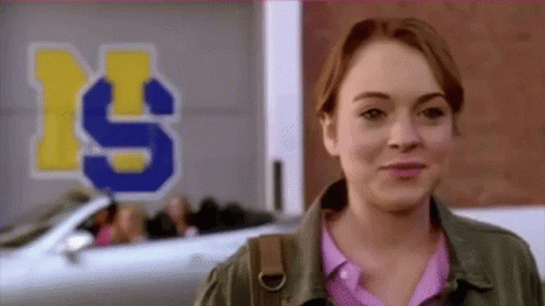 A Woman Is Smiling In Front Of A Sign That Says ' S ' On It . GIF