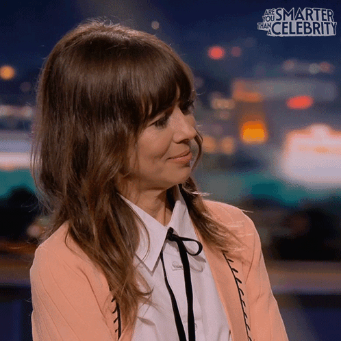 A Woman Is Smiling In Front Of A Sign That Says Smarter Than Celebrity GIF