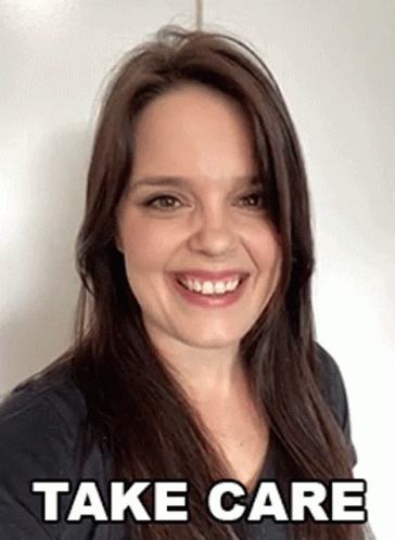 A Woman Is Smiling In Front Of A White Wall With The Words Take Care Written On It . GIF