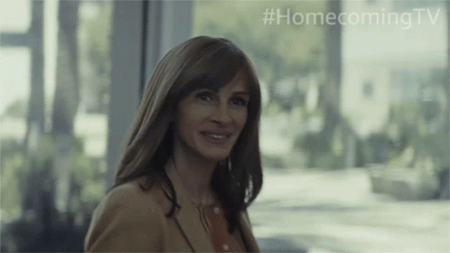 A Woman Is Smiling In Front Of A Window With #Homecomingtv Written On The Bottom GIF