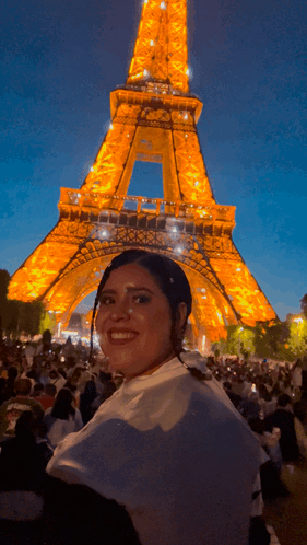 A Woman Is Smiling In Front Of The Eiffel Tower At Night GIF