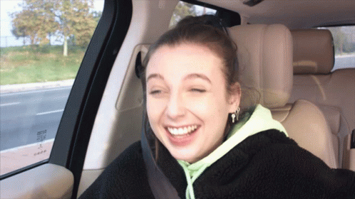 A Woman Is Smiling In The Back Seat Of A Car With A Seat Belt On GIF