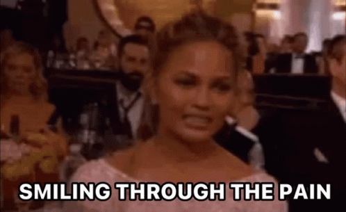 A Woman Is Smiling Through The Pain While Sitting In Front Of A Crowd . GIF