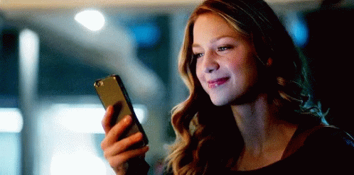 A Woman Is Smiling While Holding A Cell Phone In Her Hand . GIF