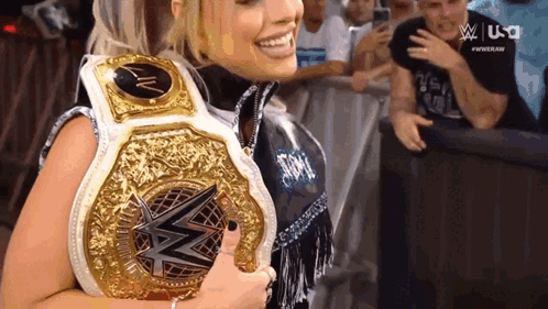 A Woman Is Smiling While Holding A Wrestling Championship Belt . GIF