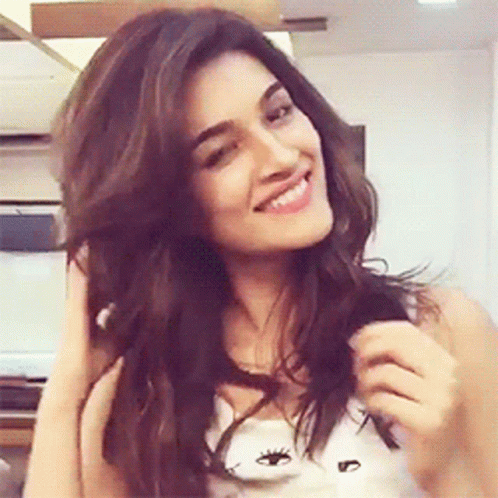 A Woman Is Smiling While Holding Her Hair And Wearing A White Tank Top . GIF