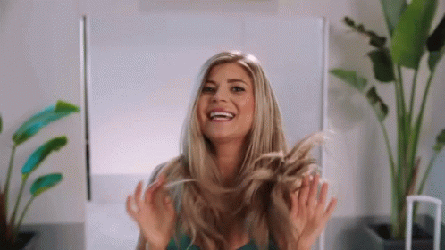 A Woman Is Smiling While Holding Her Hair In Her Hands GIF