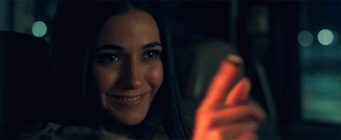A Woman Is Smiling While Looking At Her Cell Phone GIF