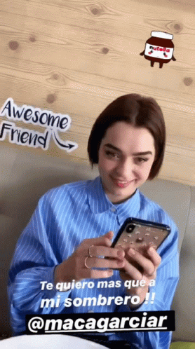 A Woman Is Smiling While Looking At Her Cell Phone With A Nutella Sticker On The Wall Behind Her GIF