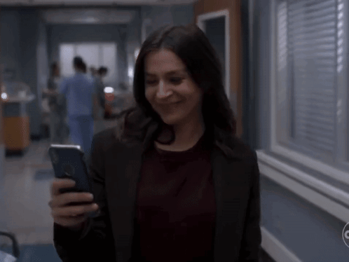 A Woman Is Smiling While Looking At Her Phone GIF