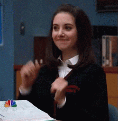 A Woman Is Smiling While Sitting At A Desk With A Book . GIF