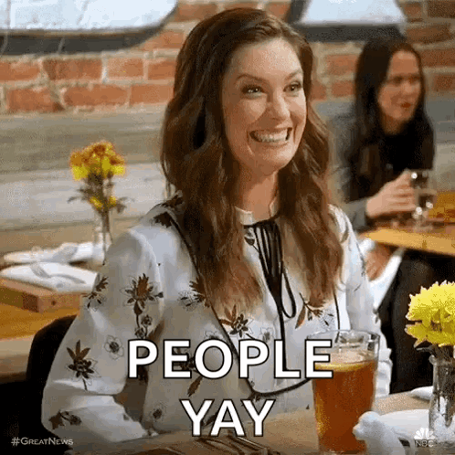 A Woman Is Smiling While Sitting At A Table With A Glass Of Beer And The Words `` People Yay '' . GIF