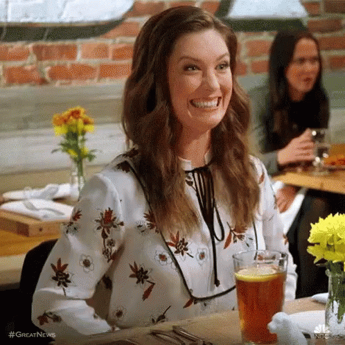 A Woman Is Smiling While Sitting At A Table With A Glass Of Beer In Front Of Her . GIF