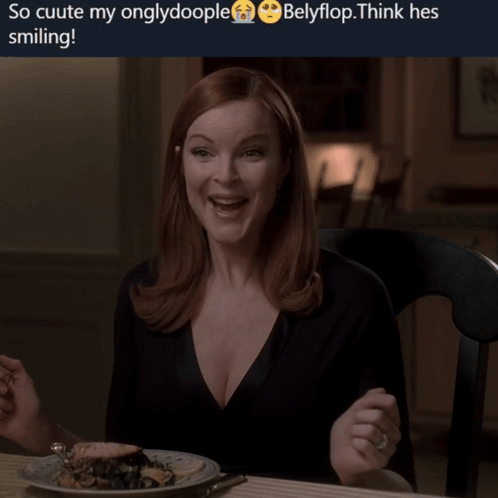 A Woman Is Smiling While Sitting At A Table With A Plate Of Food Behind Her GIF