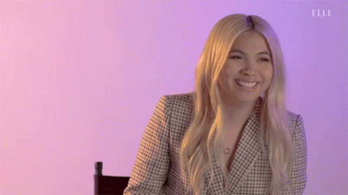 A Woman Is Smiling While Sitting In A Chair In Front Of A Purple Wall . GIF