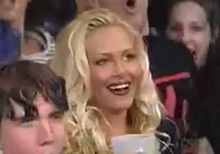 A Woman Is Smiling While Sitting In A Crowd . GIF
