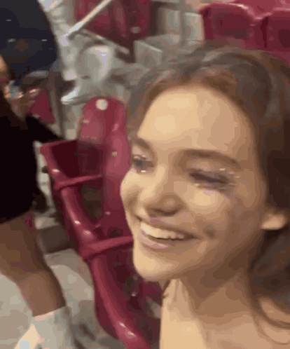 A Woman Is Smiling While Sitting In A Stadium Surrounded By Red Seats GIF