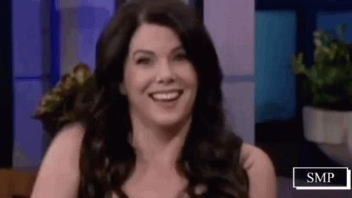 A Woman Is Smiling While Sitting On A Stage In Front Of A Purple Wall . GIF