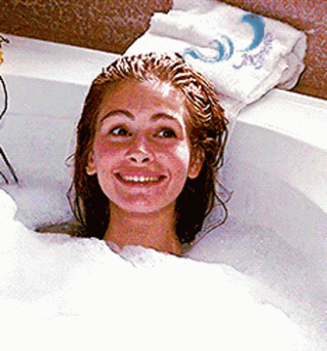 A Woman Is Smiling While Taking A Bath In A Bathtub With A Towel That Says Aquafina On It GIF