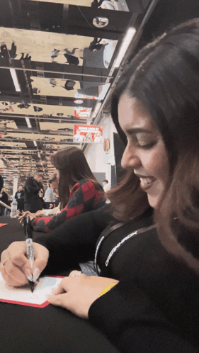 A Woman Is Smiling While Writing On A Piece Of Paper With A Pen GIF